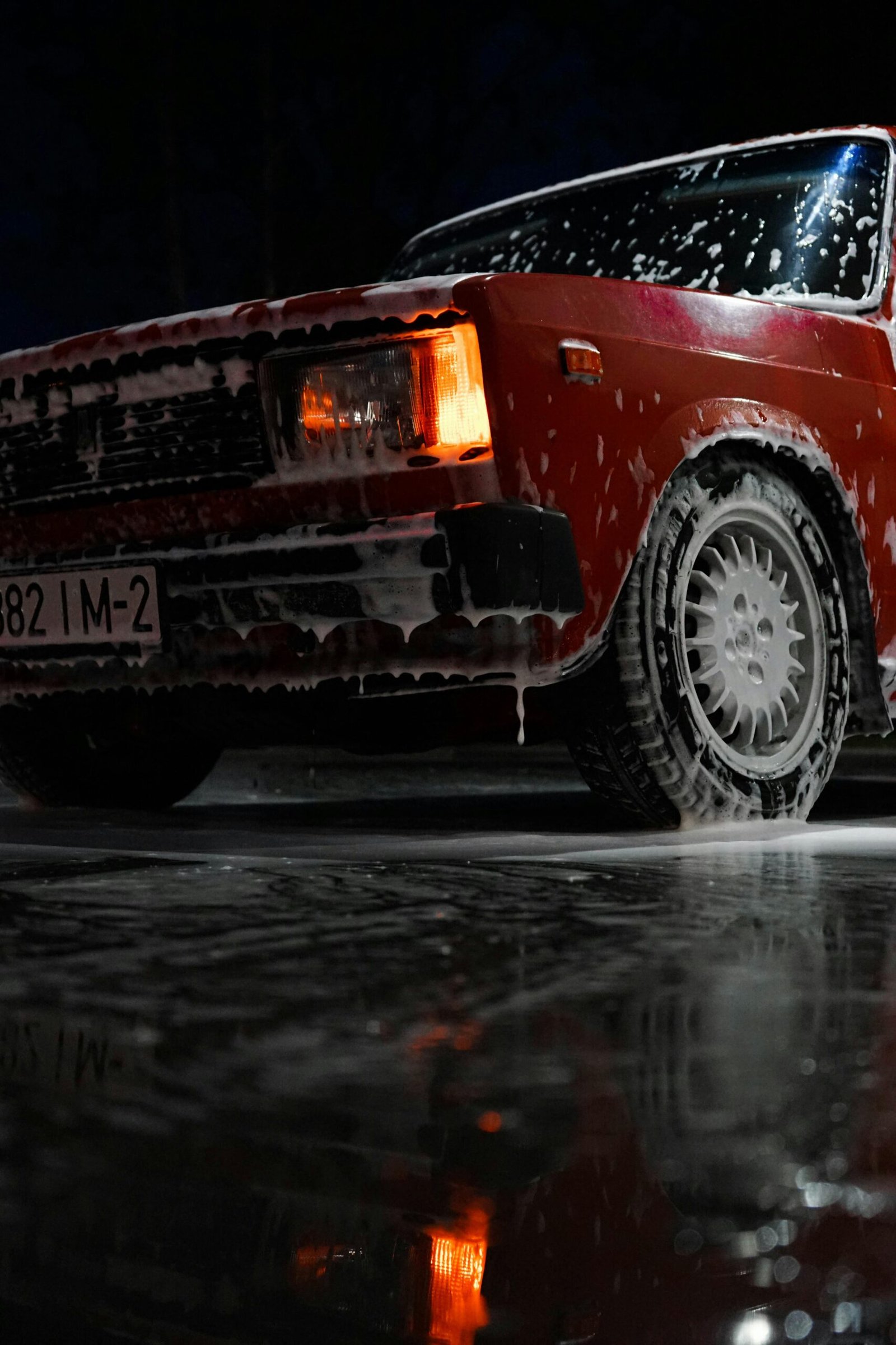 Close-up of a vintage car being cleaned at night with soapy reflections.